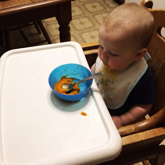 Bebé en su silla con un bol de puré naranja