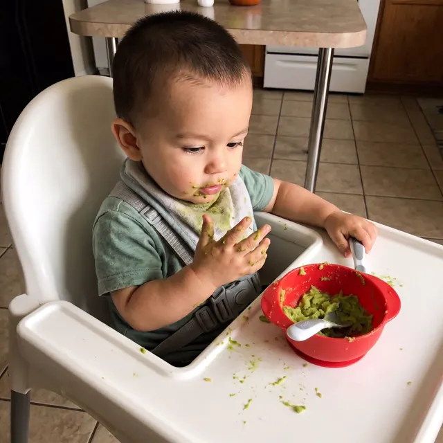 Bebé con las manos con aguacate junto a un bol rojo