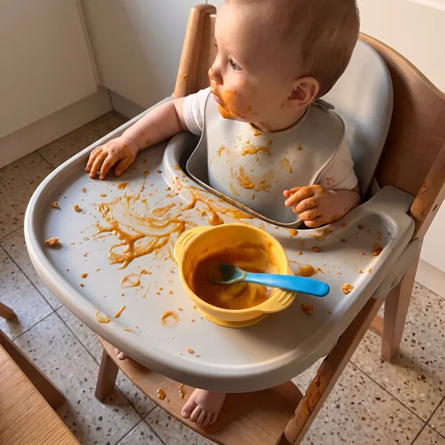 Bebé en su silla con la bandeja llena de puré